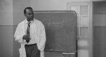 Fanon com jaleco de médico, provavelmente em aula